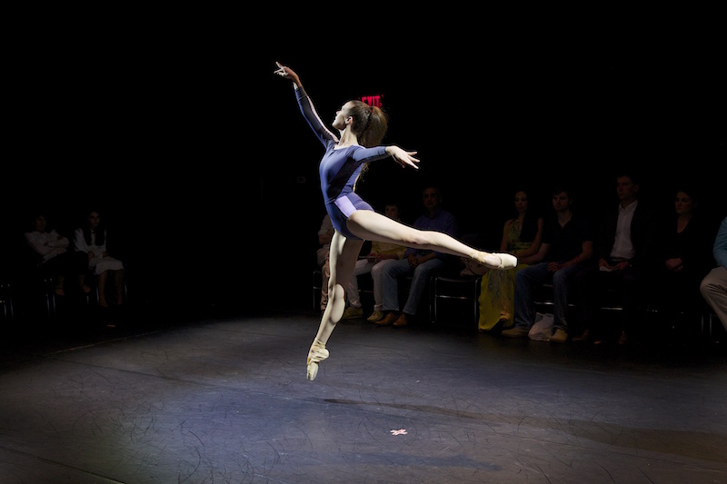 Stephanie Williams wearing a purple leotard executes a pristine arabesque sote. The photo captures her in mid air.